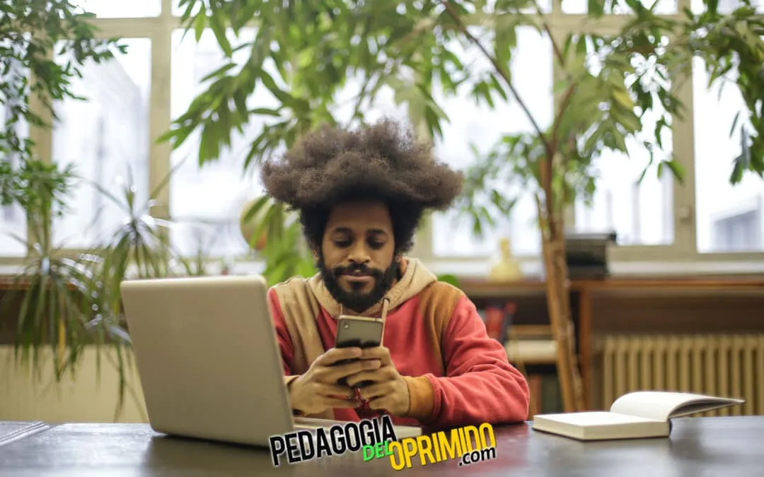 Estudiante mirando el móvil con las 5 app para ser mas productivo mientras esta trabajando en su portátil